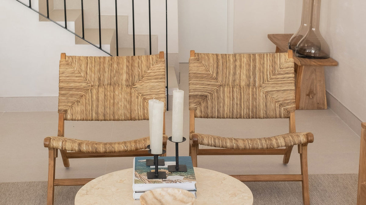 Dos butacas bajas de madera y fibra natural con mesa redonda de mármol junto a una escalera blanca