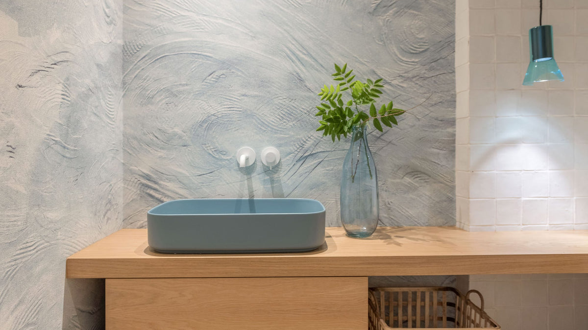 Aseo con mueble volado de madera, lavabo azul y cesto de fibra natural para las toallas