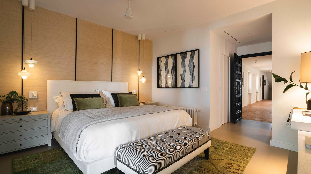 Habitación de invitados con cama de ropa blanca, cojines verdes, banco tapizado de rayas a los pies y lámparas colgantes