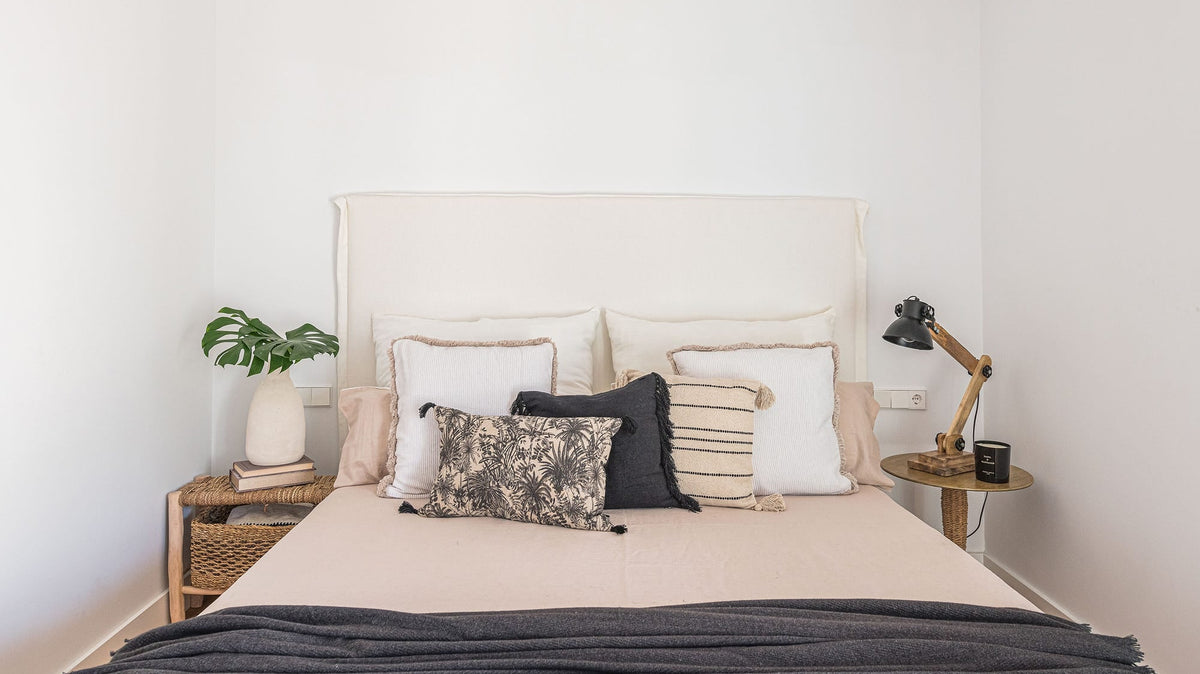 Dormitorio de estilo mediterráneo con cabecero de lino y dos mesitas de noche distintas de fibra natural