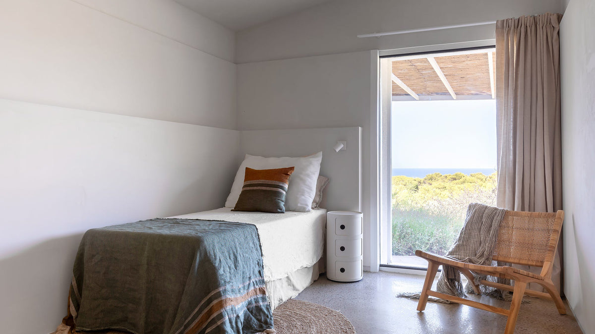 Rincón de lectura con butaca de madera junto a la ventana y vistas al mar en una casa mediterránea