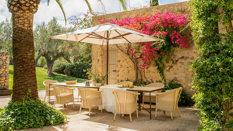 Comedor exterior mediterráneo con sillas de fibras naturales bajo una sombrilla - Pino & Jacaranda
