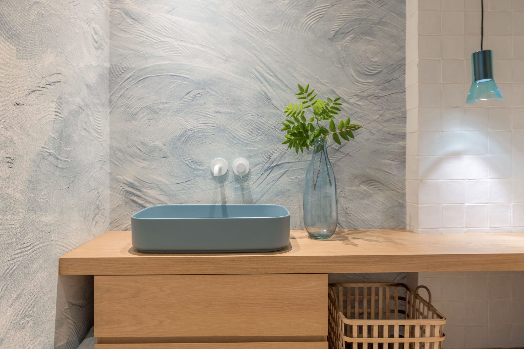 Aseo con mueble volado de madera, lavabo azul y cesto de fibra natural para las toallas