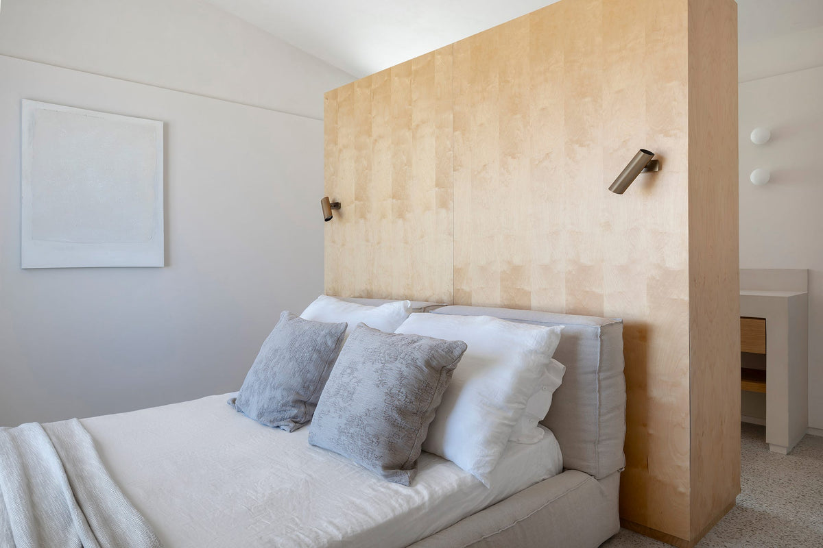 Dormitorio mediterráneo con una estructura de madera maciza que hace de cabecero, en una casa de Menorca
