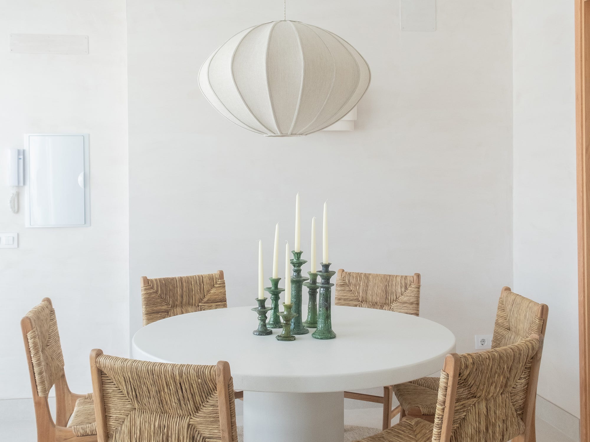 Comedor mediterráneo con mesa redonda blanca, sillas de fibra y lámpara de techo de lino