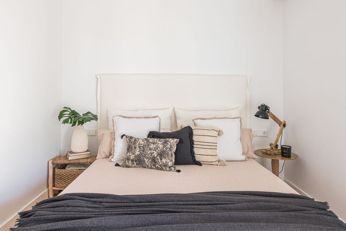 Dormitorio de estilo mediterráneo con cabecero de lino y dos mesitas de noche distintas de fibra natural