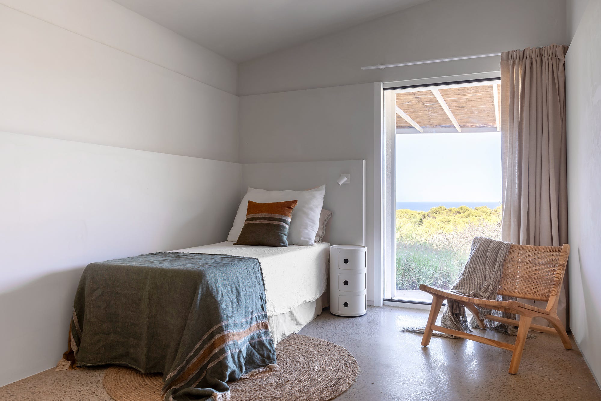 Rincón de lectura con butaca de madera junto a la ventana y vistas al mar en una casa mediterránea
