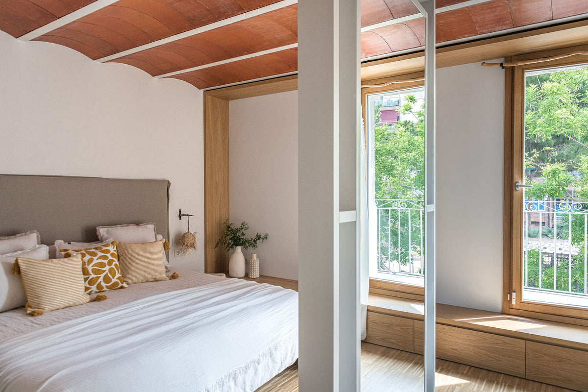 Dormitorio con techo de volta catalana, ropa de cama blanca y cojines en tonos mostaza
