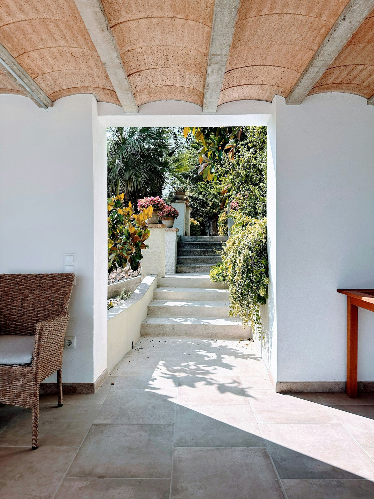 Entrada de casa mediterránea con techo de bóveda de ladrillo, suelo de piedra y puerta abierta a un patio con plantas