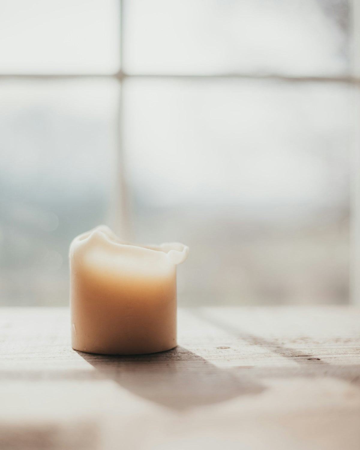 Vela de cera natural sobre una mesa de madera junto a una ventana con luz suave