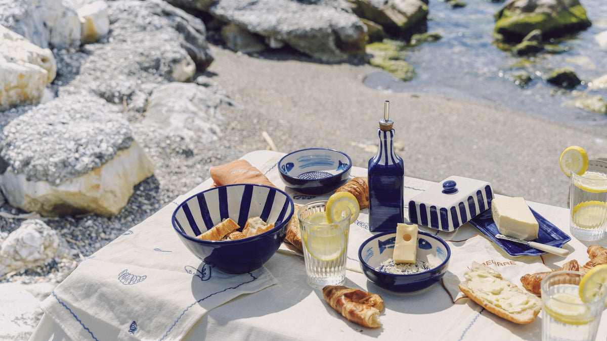 Mesa junto al mar con cerámica artesanal azul y blanca, pan y limones